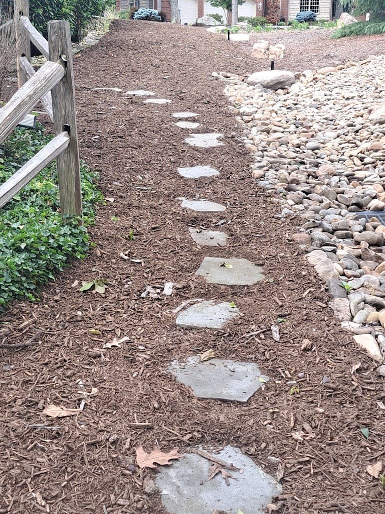 Stone paver walkway set in a fresh mulch bed with a rock border